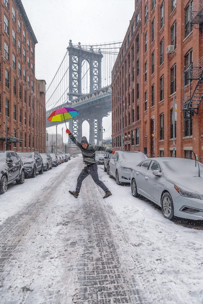 Colorful umbrella in a snowy DUMBO street framed by the Manhattan Bridge